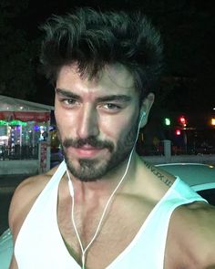 a man with headphones on standing in front of a car at night, wearing a tank top