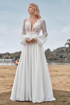 a woman in a long white dress standing on the grass with her hands clasped to her chest