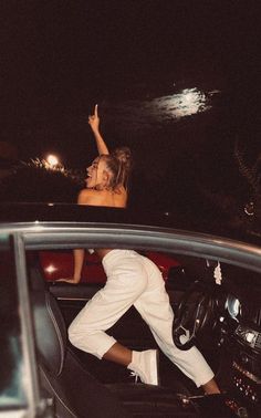 two people sitting in the back of a car at night, one person raising her hand