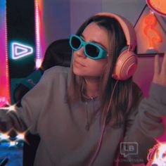 a woman wearing headphones and sunglasses in front of neon lights with her hands up