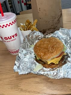 a hamburger and fries are on the table next to a cup of soda or coffee