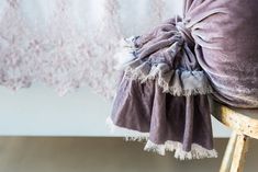 the back of a chair with a purple pillow on it and a lace curtain in the background