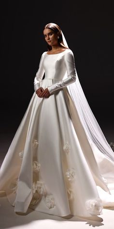 a woman in a white wedding dress with long sleeves and flowers on the skirt is standing