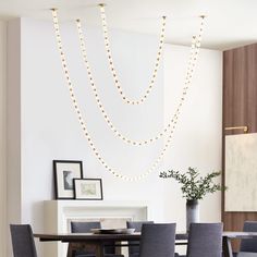 a dining room table and chairs with string lights hanging from the ceiling above it, in front of a white wall