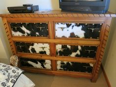 a dresser with cow hide drawers in front of a tv