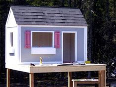 a doll house is sitting on top of a wooden table in front of some trees