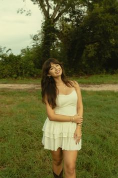 a woman standing in the grass with her arms around her waist and smiling at the camera