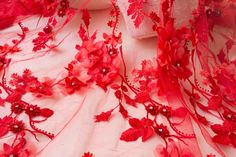 red lace with flowers and pearls on it is laying on a white surface next to a pillow