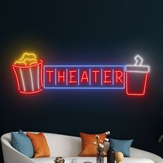 a neon sign that says theater with popcorn buckets and drinks on the table next to it