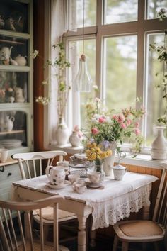 a table with flowers and tea cups on it in front of a window