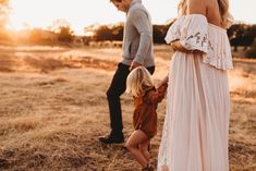 a man and woman holding hands while standing in a field with a toddler girl