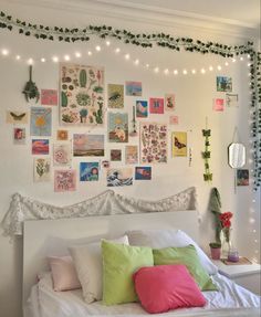 a white bed topped with lots of pillows next to a wall covered in pictures and plants