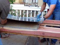 two men working on an outdoor table being built with wood and metal sheet covering it