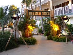 an entrance to a tropical resort surrounded by palm trees and other greenery at night