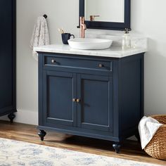 a bathroom vanity with a marble top and dark blue cabinetry, along with a wicker basket on the floor