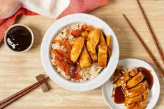 a plate with rice, meat and sauce next to chopsticks on a table