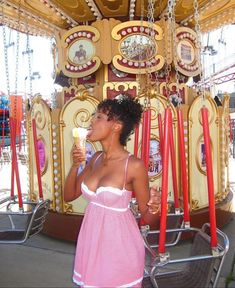 a woman eating an ice cream cone in front of a merry - go - round