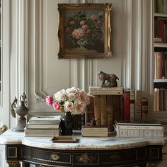 a table topped with books and vases filled with flowers next to a painting on the wall