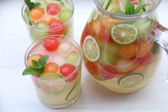 two pitchers filled with fruit and mint garnish on top of a white table