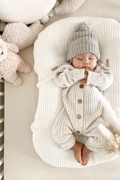 a baby sleeping in a white blanket next to stuffed animals