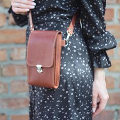 a woman wearing a black dress holding a brown leather handbag in her right hand