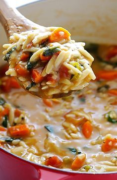 a ladle full of pasta and vegetables being held by a wooden spoon over a red pot