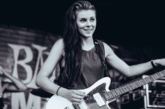 a woman standing next to a guitar and holding it in her hand with both hands