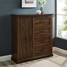 a wooden cabinet with two drawers and a vase on top in a blue walled room