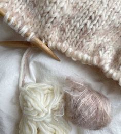 yarn and knitting needles on top of a white blanket next to a ball of yarn