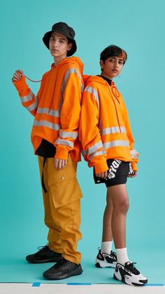 two young men in orange jackets and black shorts standing next to each other on a blue background