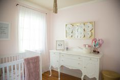 a baby's room with pink walls and white furniture