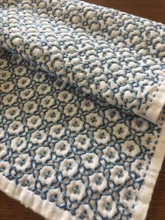 two pieces of blue and white crocheted fabric on a wooden table with wood flooring