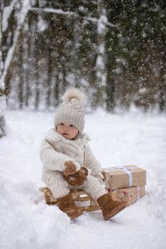 a small child sitting in the snow on a sled with a teddy bear and gift box