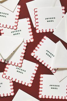 many white envelopes with red writing on them are scattered around each other and one has a piece of paper in the middle that says joyeux noel