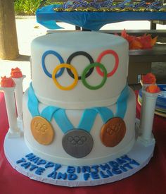 a white cake with blue ribbon and olympic rings on top