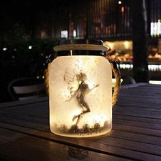 a lit up jar sitting on top of a wooden table with a fairy image in it