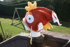 a knitted fish hat sitting on top of a wooden fence next to a green field