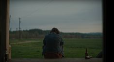 a person sitting on a porch looking out at the grass and trees in the distance