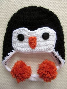 a crocheted penguin hat with orange pom poms