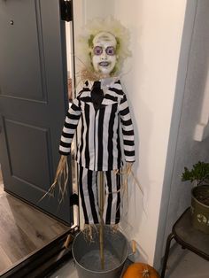 a creepy clown dressed in black and white striped clothes standing next to an orange pumpkin