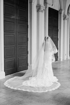 a woman in a wedding dress and veil standing on the floor with her back to the camera