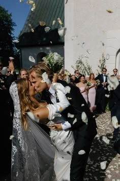 a bride and groom are kissing in front of a group of people who are throwing confetti into the air