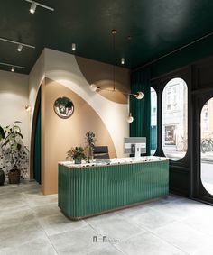 a green and white reception desk in front of two large windows with circular lights hanging from the ceiling