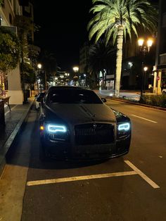 a black car parked on the side of a street next to a palm tree at night