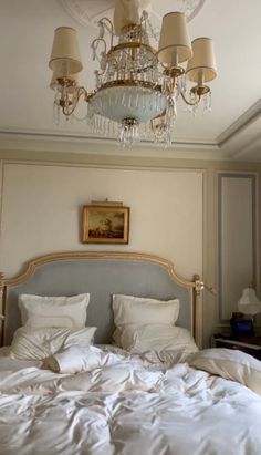 a bedroom with a chandelier hanging from the ceiling and white linens on the bed