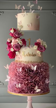 a three tiered cake with pink flowers and butterflies on top is decorated with the number one