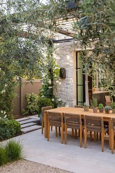 an outdoor dining area with wooden table and chairs, surrounded by greenery on either side