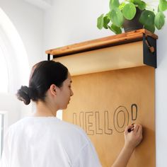 a woman writing on a wall with a plant in the back ground and an orange box behind her