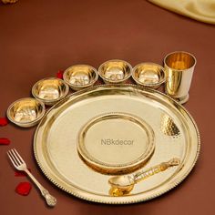 there is a gold plate with silver cups and spoons on the table next to it