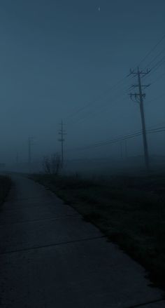 an empty road in the fog with telephone poles and power lines on either side at night